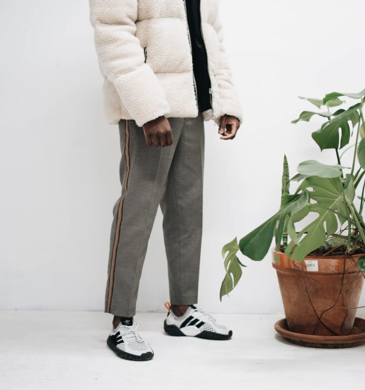 Ung man med en vit dunjacka och gråa byxor modellerar i en butik.